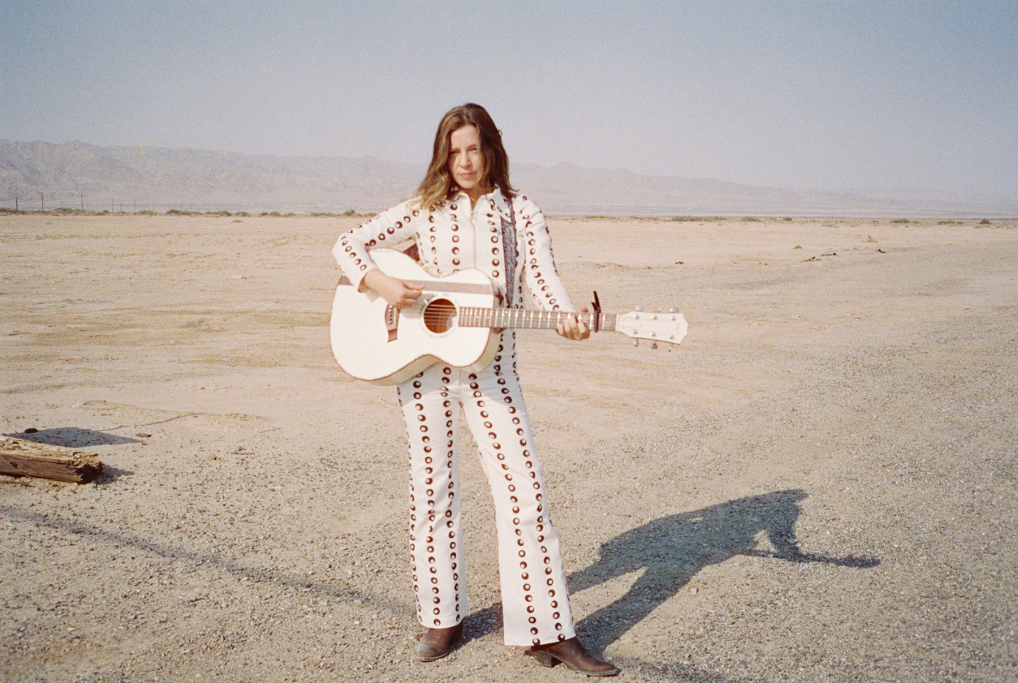 Artist Jade Bird standing with guitar in desert
